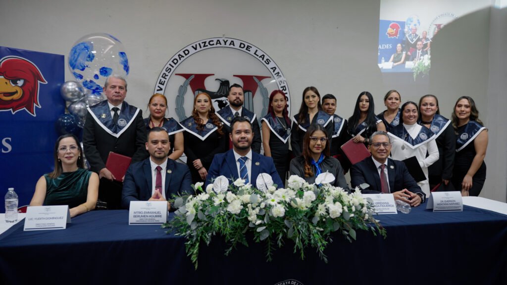 Fotografía grupal de una ceremonia de graduación o titulación de la Universidad Vizcaya En Línea (UVAL). Muestra a un grupo de 10 graduandos de pie, vestidos con togas y estolas blancas y negras, posando detrás de una mesa principal. En la mesa están sentadas 5 personas: tres hombres con traje oscuro y corbata y dos mujeres. La mesa está adornada con un centro de mesa floral grande de rosas blancas. Al fondo se distingue el escudo de la universidad y hay una pantalla en la esquina superior derecha que muestra imágenes de un evento académico.