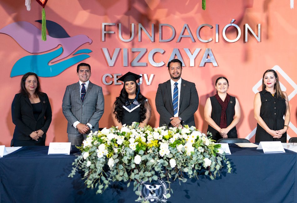 Integrantes del presídium y autoridades académicas junto a una graduada en la ceremonia de la Universidad Vizcaya en Línea 2023-2026. Posan frente a un muro con el logo de la Fundación Vizcaya y un arreglo floral blanco, celebrando el éxito académico.